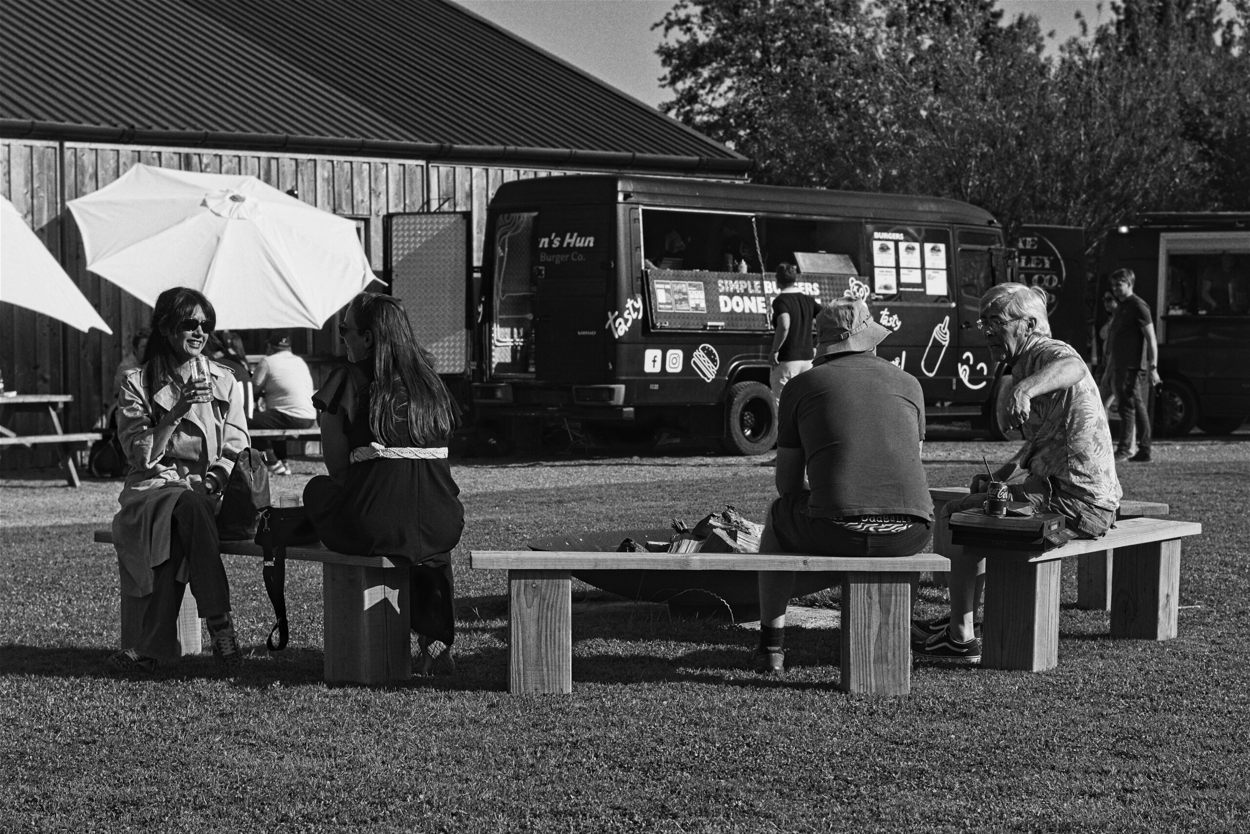 People sat on a bench with the GBH food truck in the background at an event in the South West